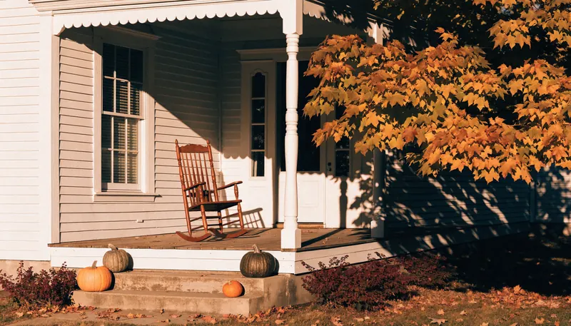 The front porch of a classic American farmhouse with a rocking chair and pumpkins on the steps in autumn The front porch of a classic American farmhouse with a rocking chair and pumpkins on the steps in autumn
