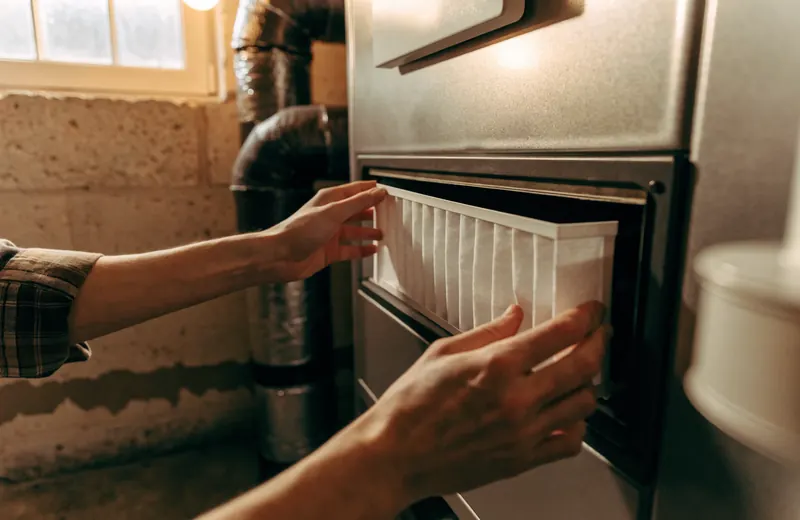 A homeowner's hands sliding a fresh pleated furnace filter into the filter slot of a basement furnace A homeowner's hands sliding a fresh pleated furnace filter into the filter slot of a basement furnace