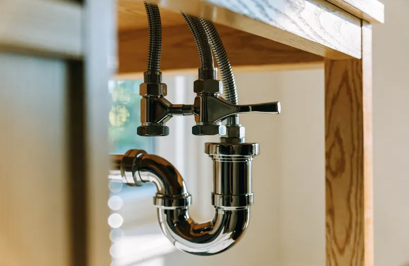 The inside of a sink cabinet showing a chrome P-trap and two shutoff valves with braided supply lines The inside of a sink cabinet showing a chrome P-trap and two shutoff valves with braided supply lines